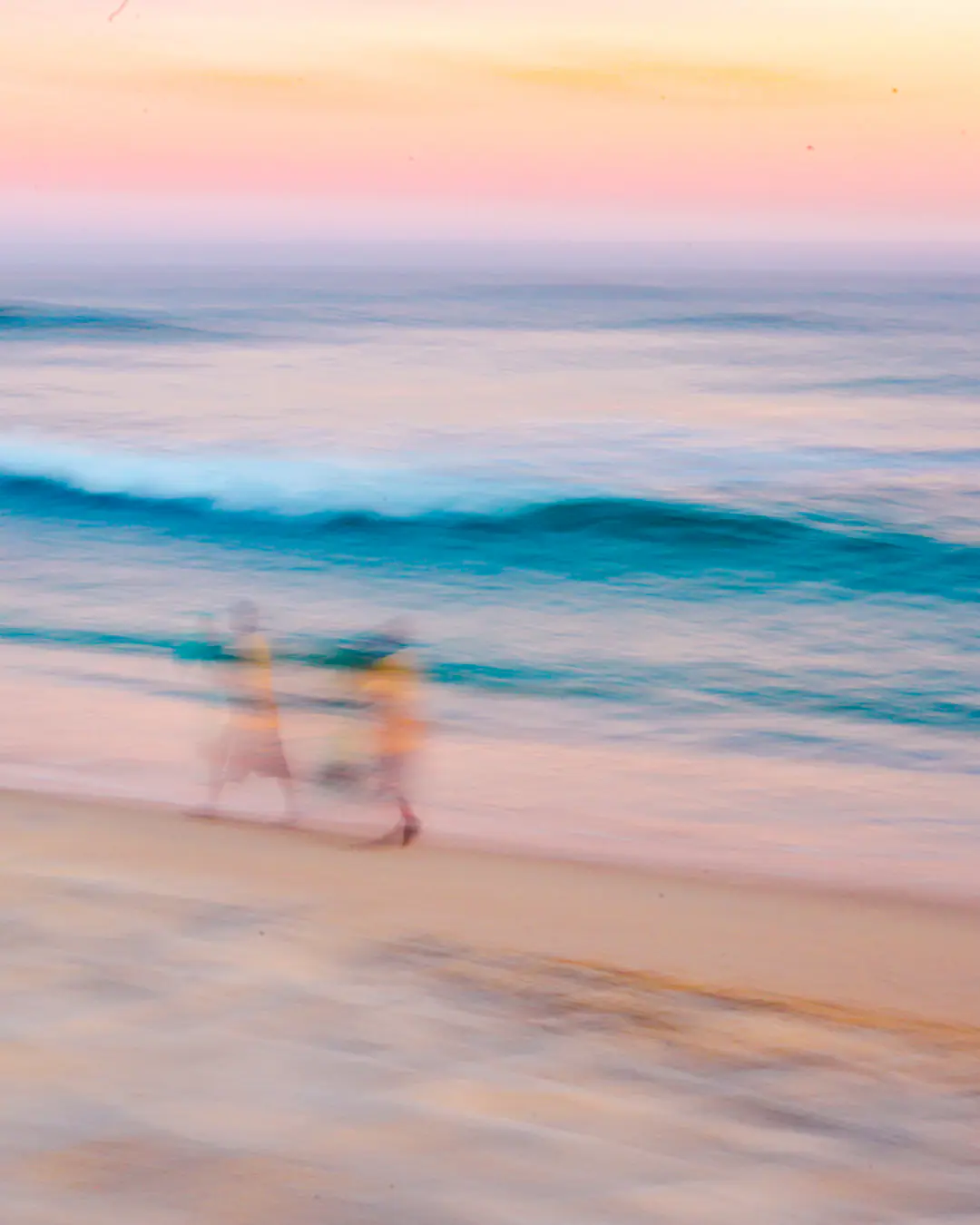 Long exposure of the sea in pink and blue, with two figures blurred on the shore