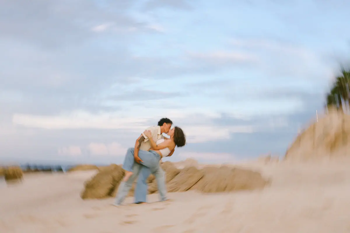 He dips her into a kiss on the rocks by the sand