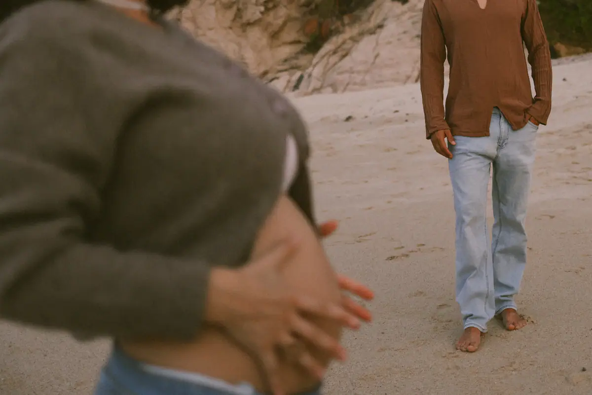 Her belly in the foreground, him standing barefoot behind her
