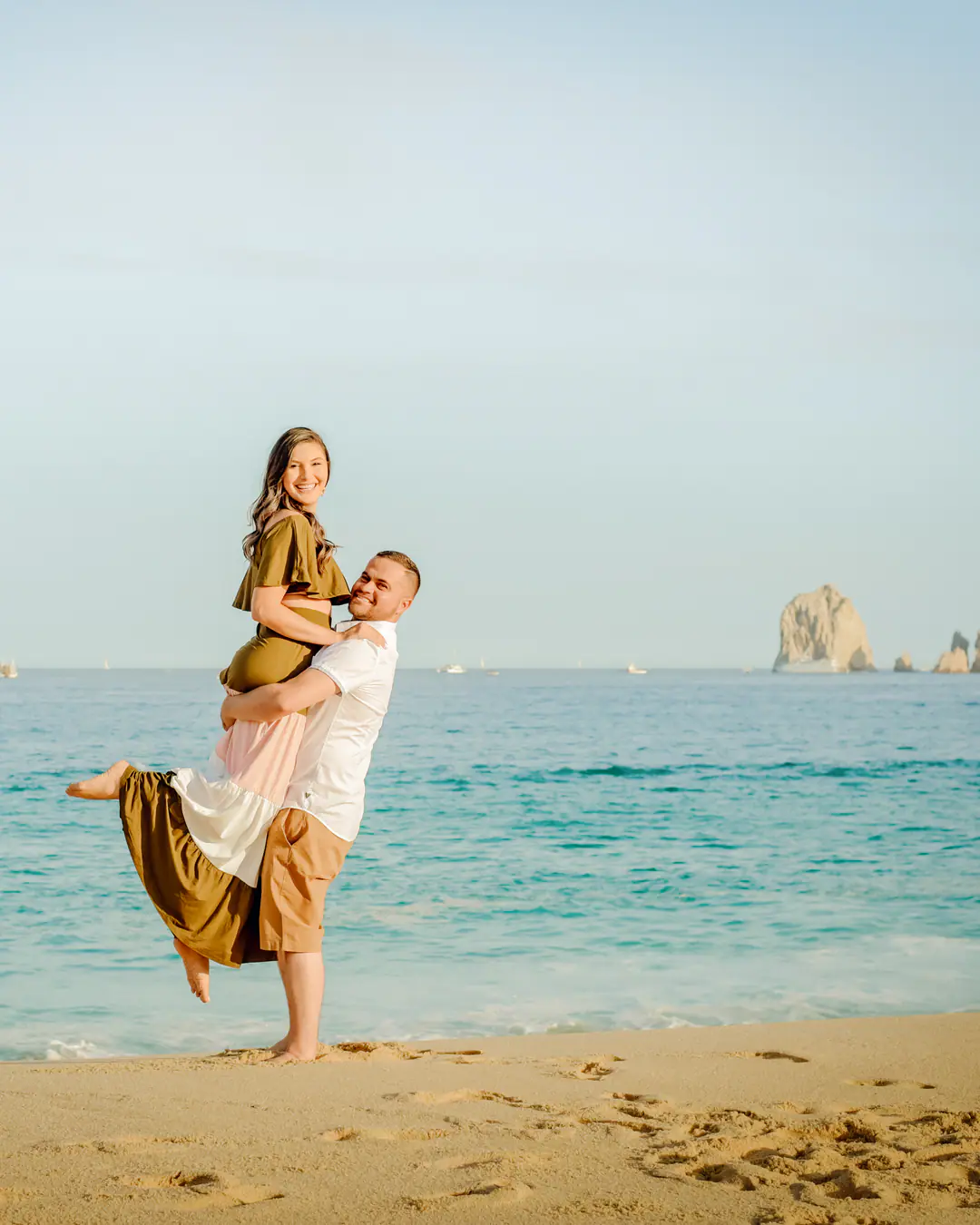 He lifts her by the sea with El Arco on the horizon