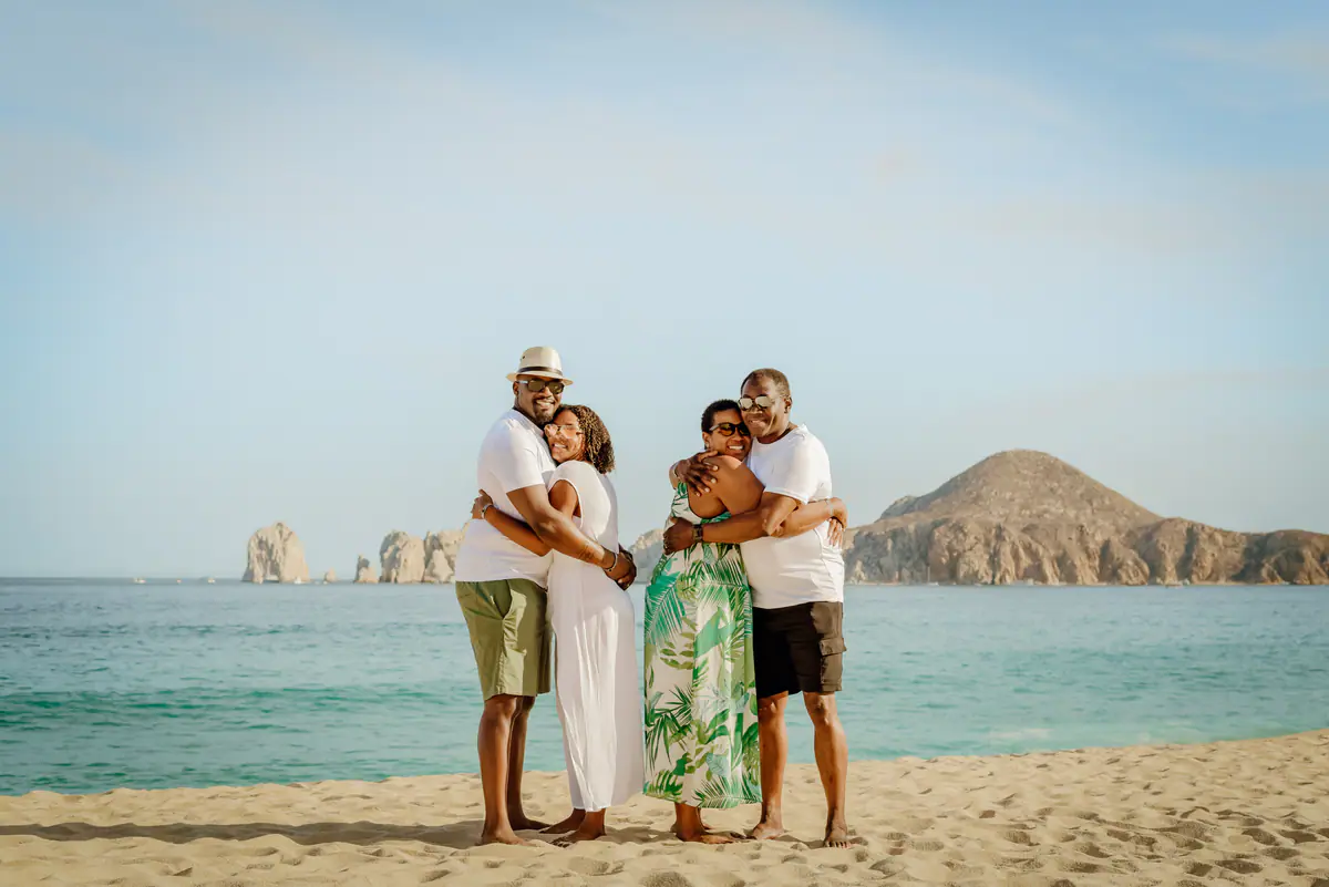 Two couples hugging on the beach with El Arco in the distance
