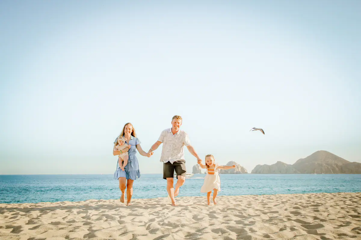 A family running on the beach with El Arco behind them